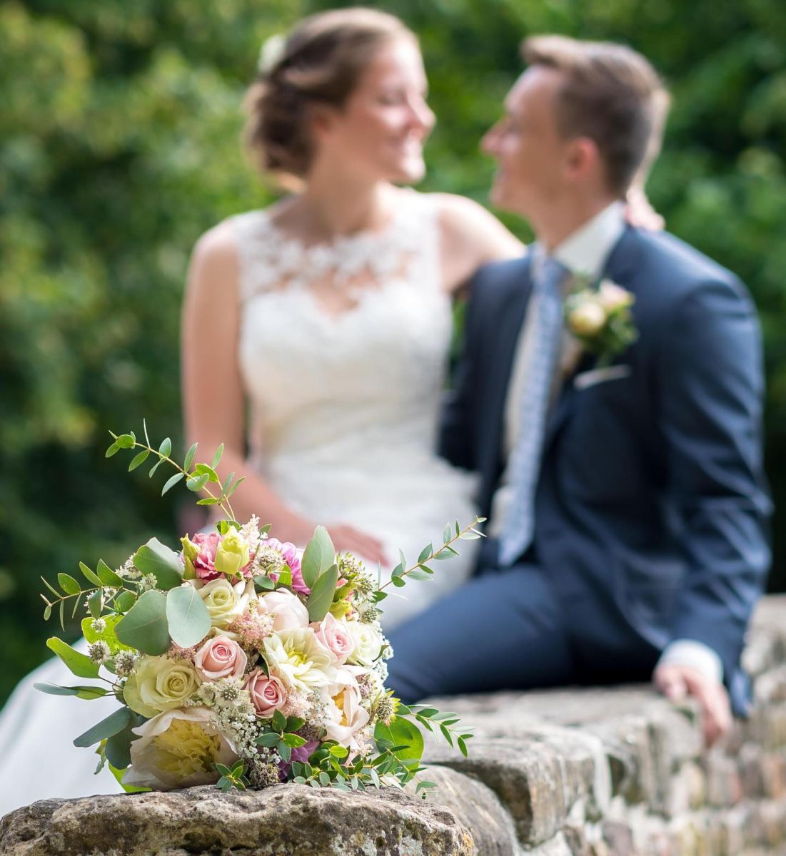 Bruidspaar met bruidsboeket op de voorgrond en de bruidegom draagt een herencorsage Mies Bloemen