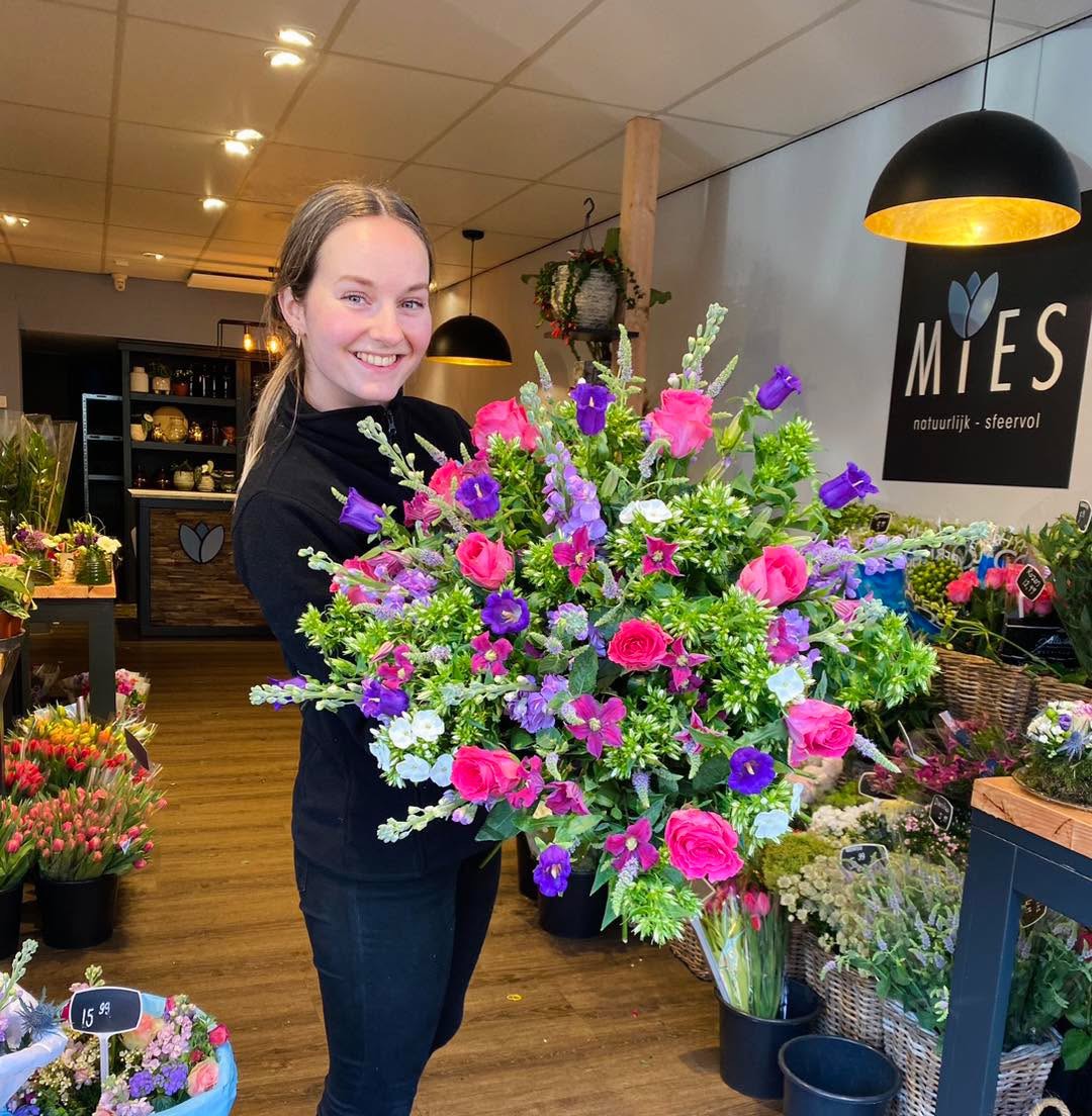 Medewerker van Mies Bloemen met een boeket in paars, roze en groen
